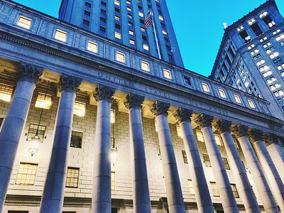 Front of Thurgood Marshall Courthouse, U.S. Court of Appeals for the Second Circuit, at night with lighting. View looking up at the front of a courthouse with several tall pillars, lit up by lights.